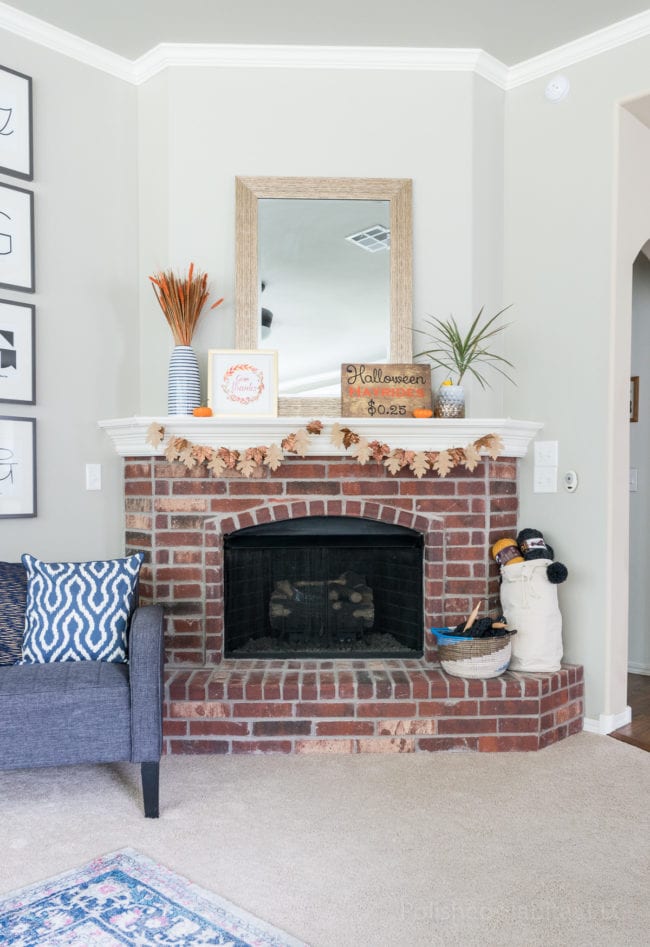 Brick fireplace with white mantel decorated for fall.