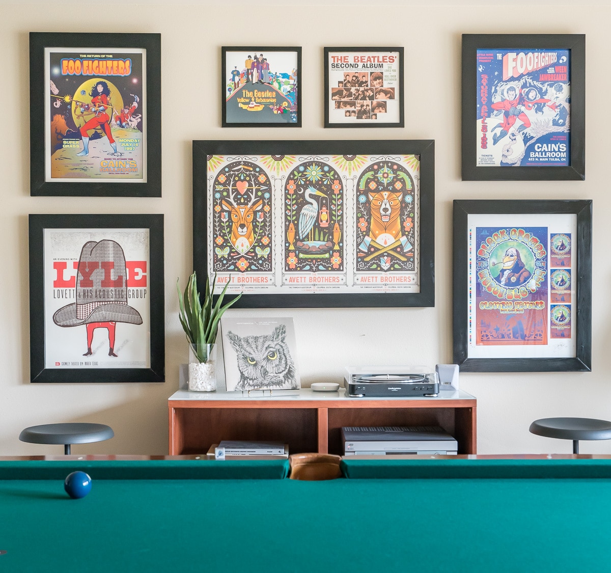 Colorful concert poster gallery wall in in game room with record player and pool table