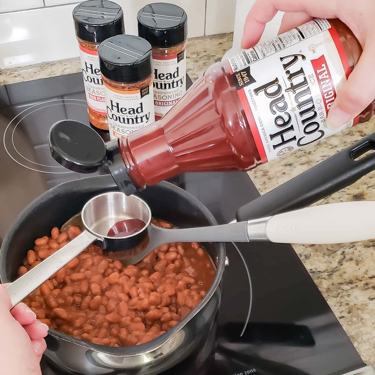 Baked beans on stove with Head Country BBQ Sauce being poured in