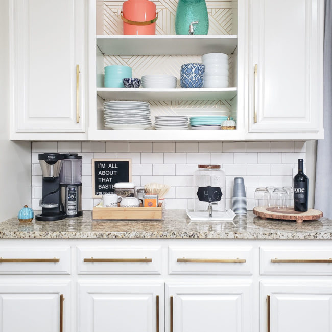 White kitchen cabinets with long gold pulls and a drink station on the counter