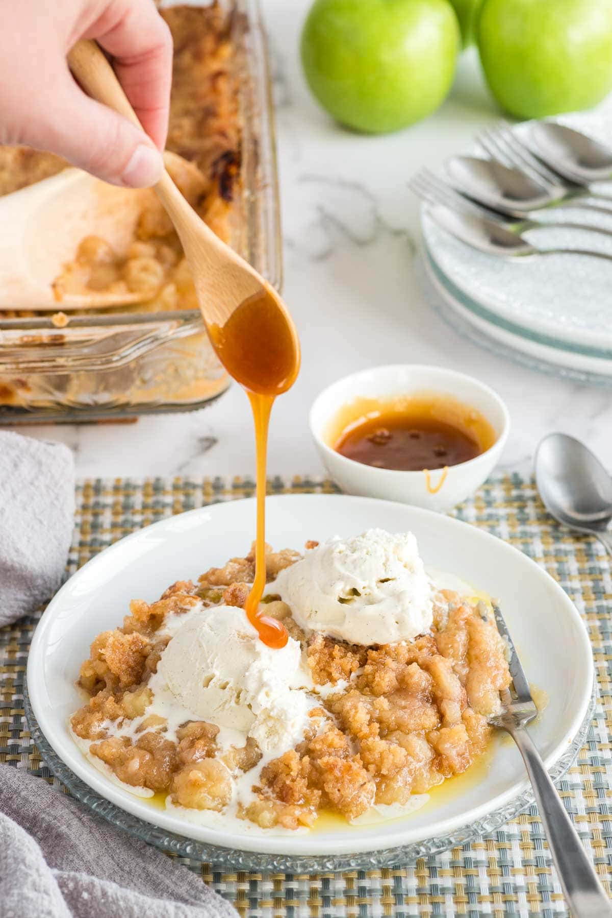 Apple crisp in white bowl with vanilla ice cream and caramel drizzle.