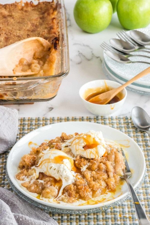 Apple crisp in white bowl with vanilla ice cream and caramel drizzle.