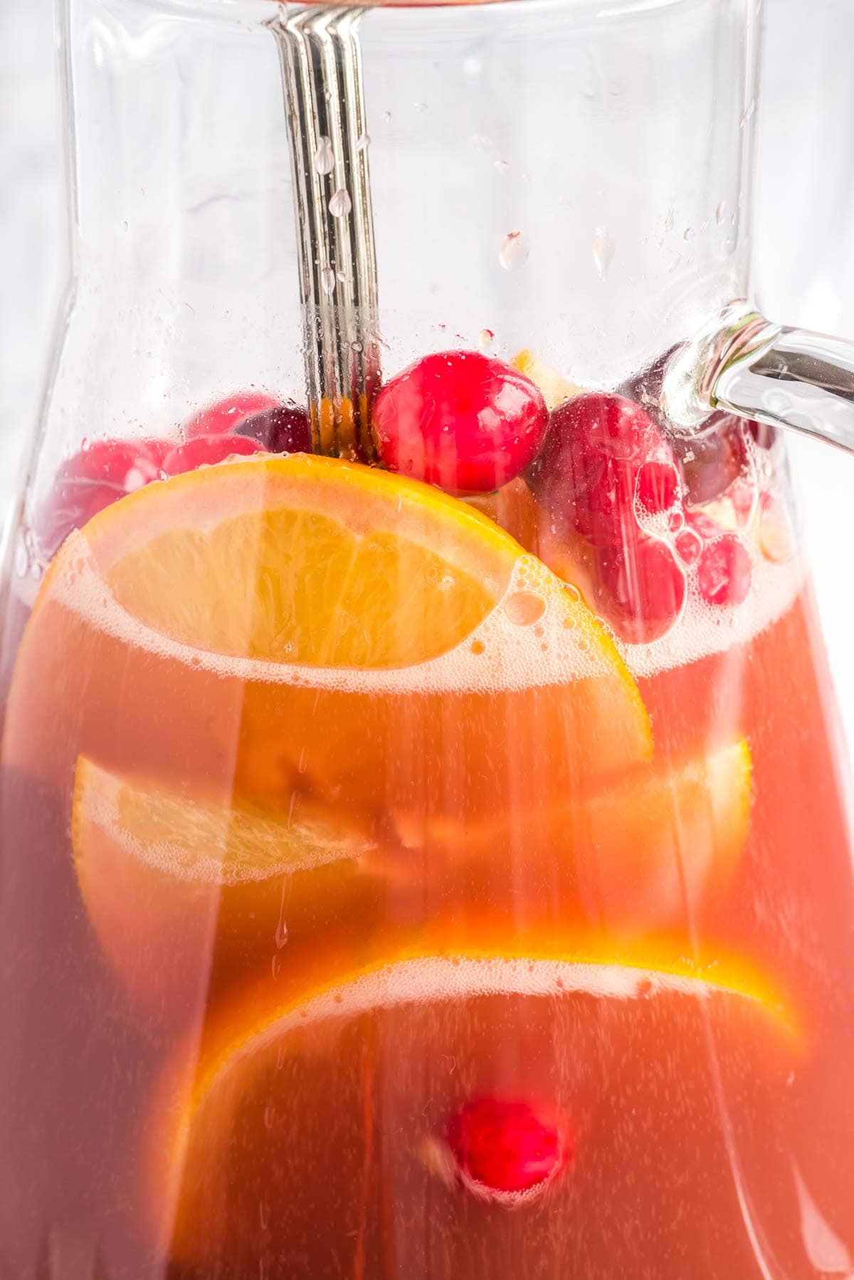 Orange slices and cranberries floating in pitcher of mimosas