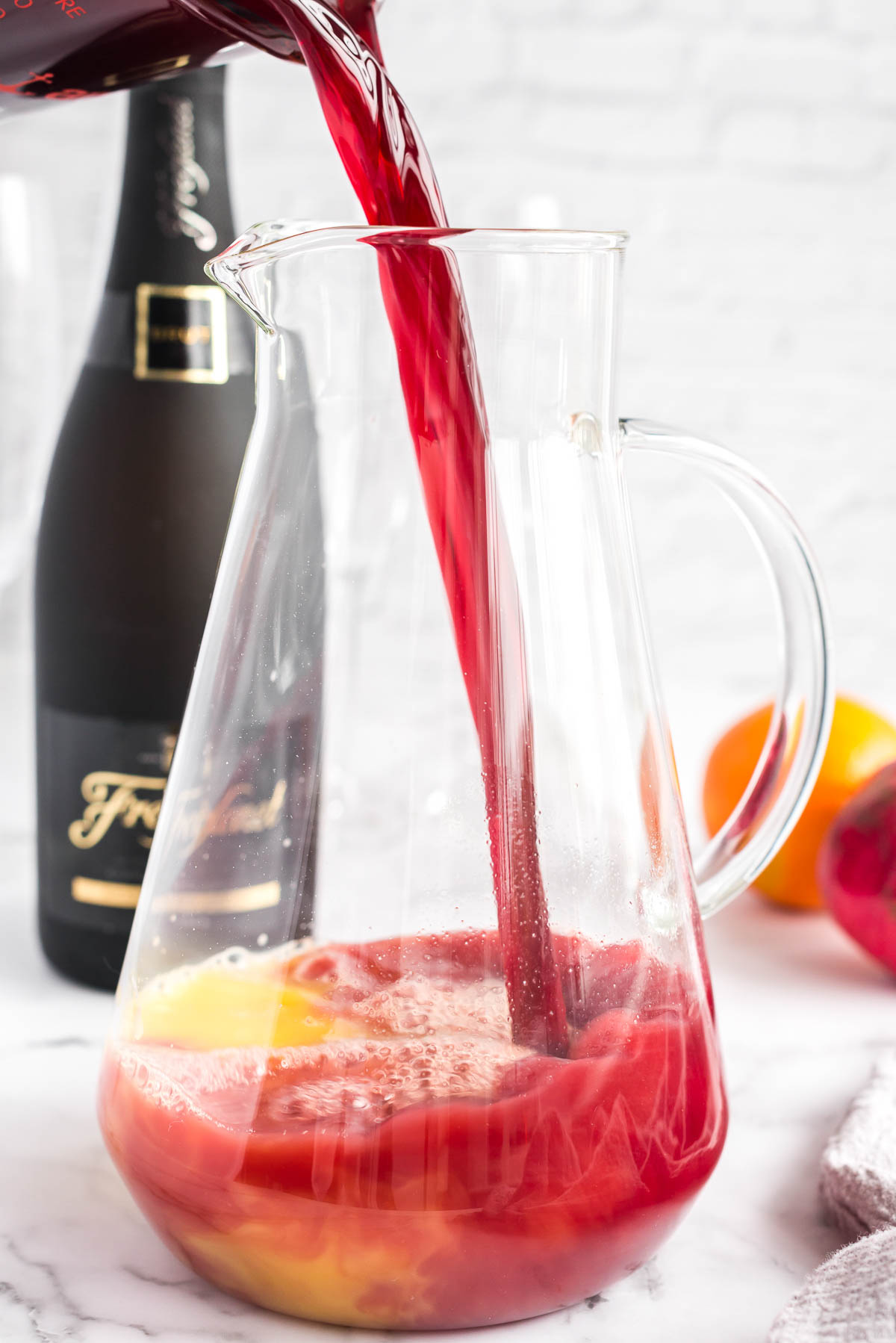 Pomegranate juice poured into a clear pitcher of orange juice for mimosa