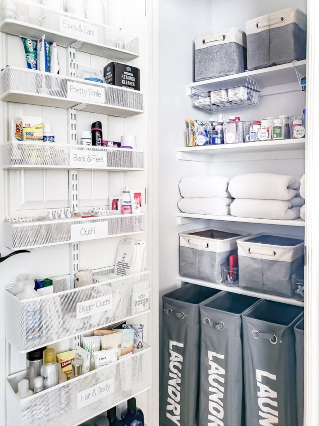 white organized linen closet with organization on the door and gray bins on the shelves.