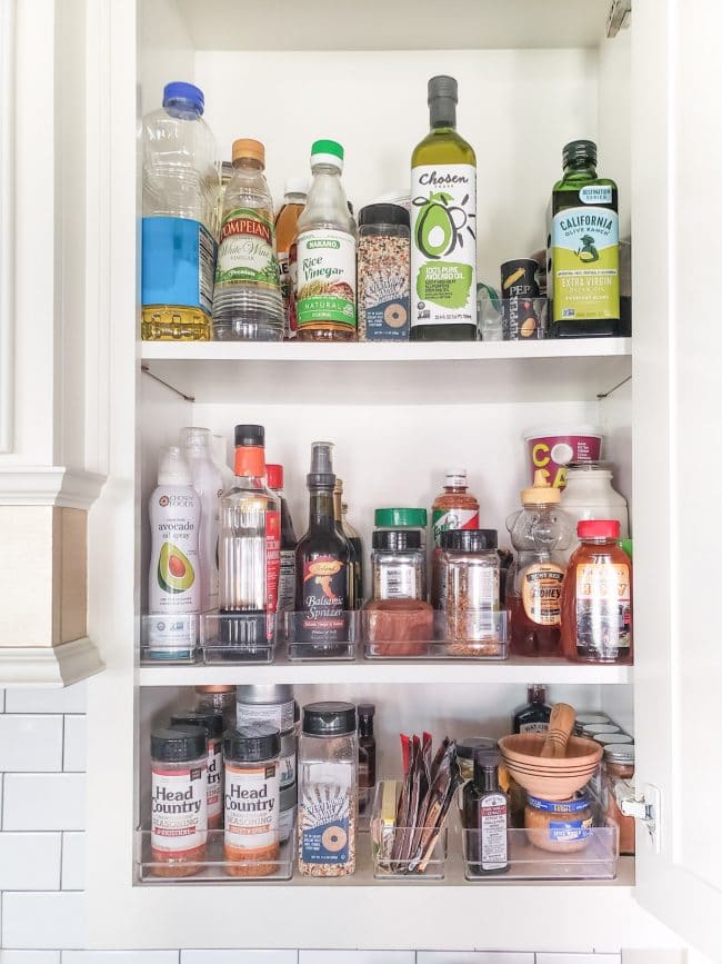 White cabinet full of cooking items like spices, oils, and vinegars