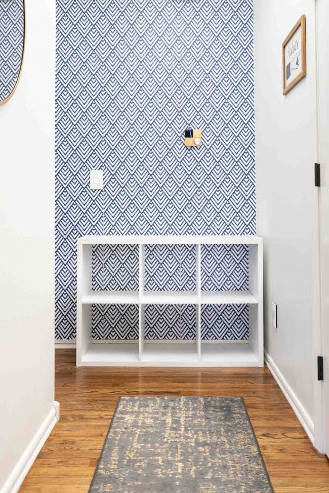 Hallway with wood floors, and white cube storage organizer against geometric blue and white wall.