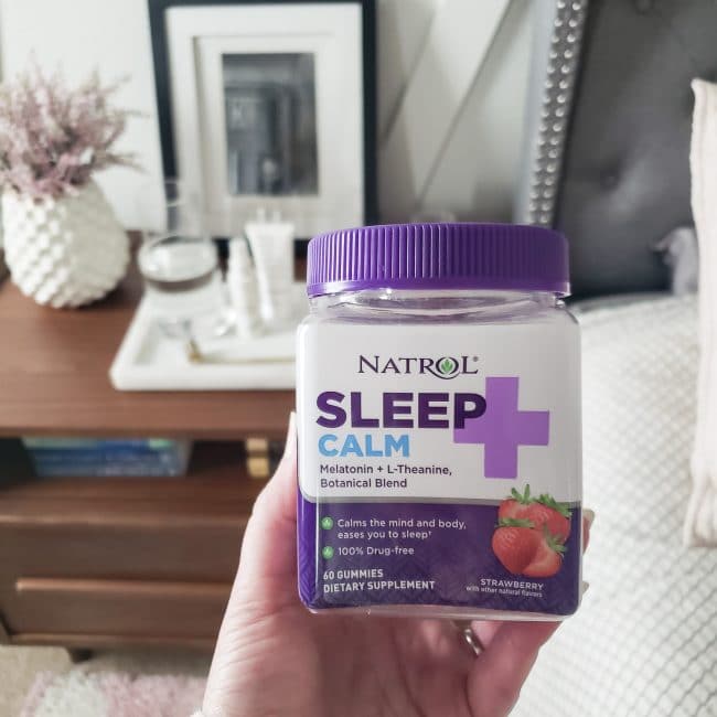 hand holding bottle of Natrol Sleep+ Calm in front of wood nightstand