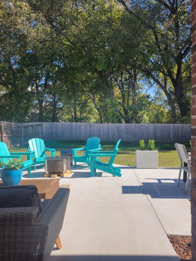 Backyard with teal chairs and tall trees in background