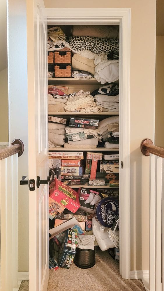 Messy linen closet with piles of games and towels